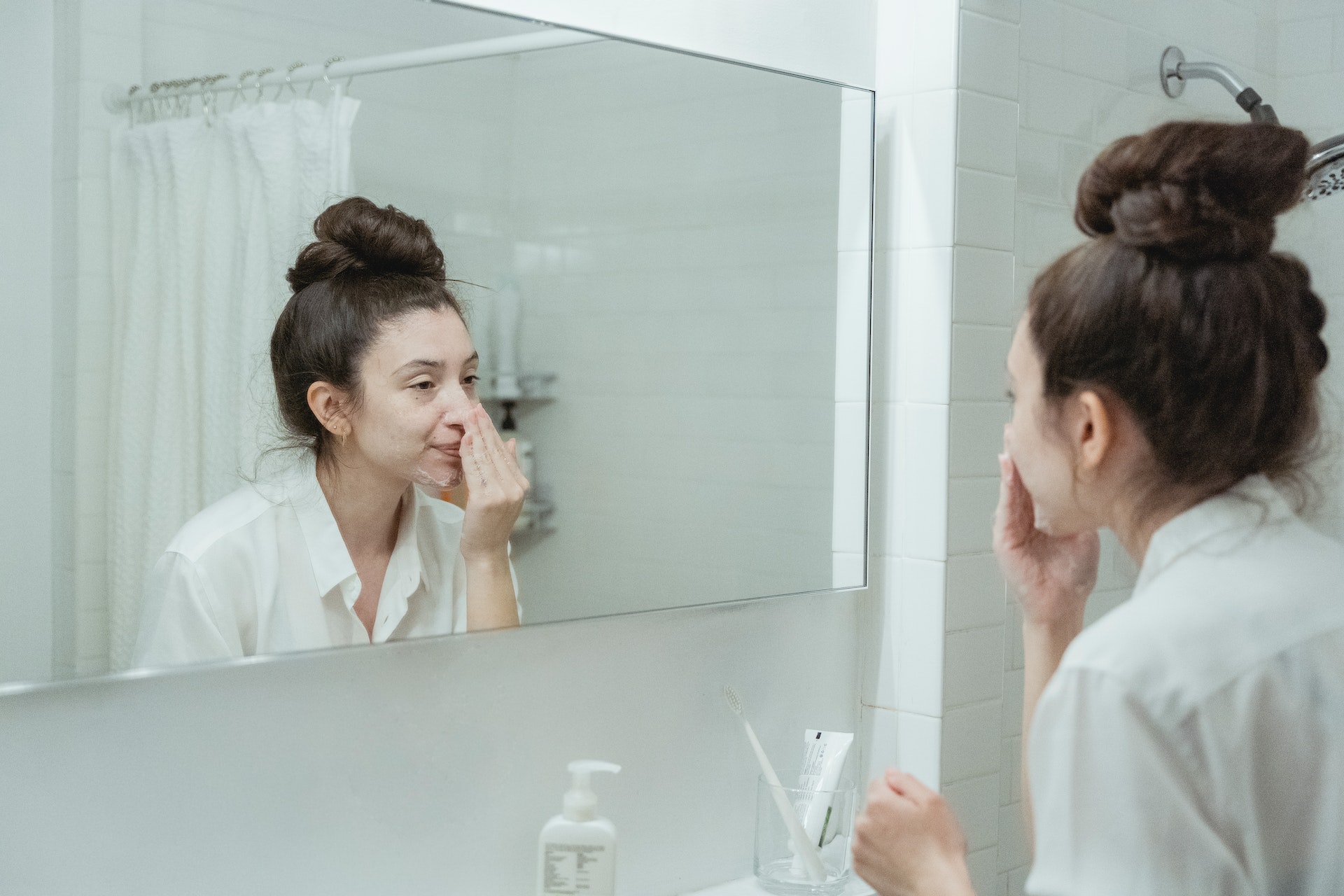 woman-in-a-white-bathroom-washing-face-and-looking-at-the-mirror